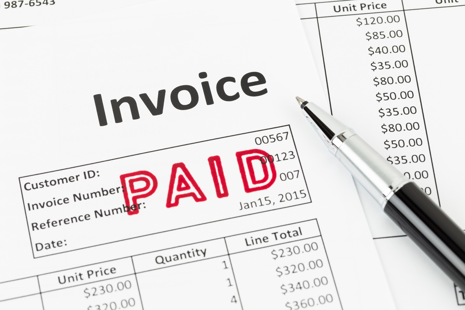 Invoice and pen with paid stamp; invoice is mock-up